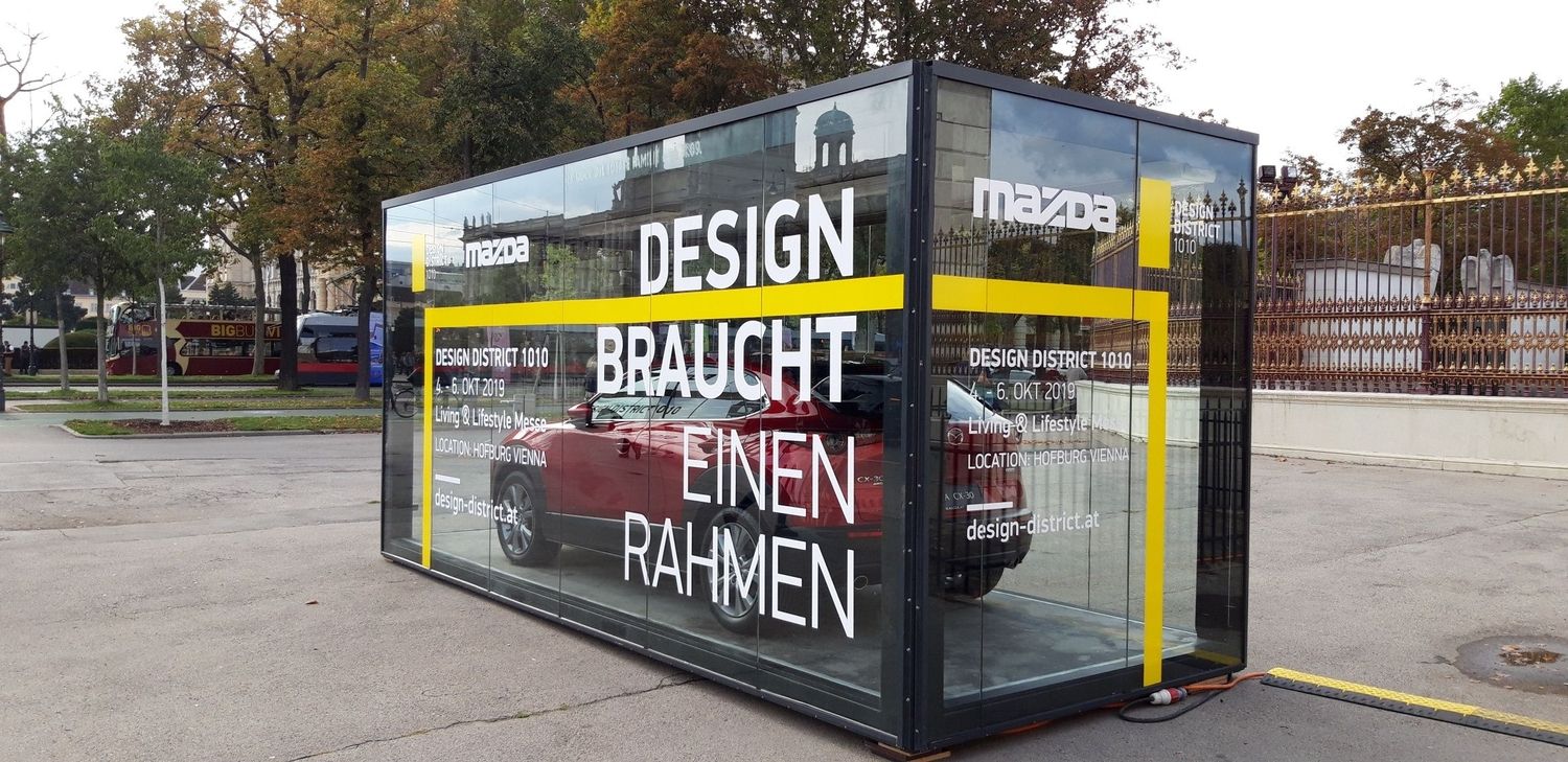 Ein Promotioncontainer mit Glaswänden und einem Auto im inneren